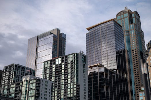A cluster of modern skyscrapers with reflective glass facades set against a cloudy sky.