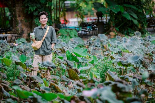 Free Woman standing in a lush, leafy garden holding a drink, surrounded by greenery. Stock Photo