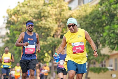 Free Marathon runners in vibrant attire participating in a city race holding hydration bottles. Stock Photo