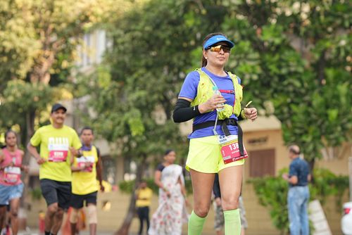 Free A woman jogs confidently in a city marathon, surrounded by other runners and greenery. Stock Photo