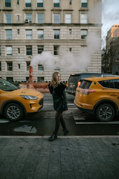 Woman walks on New York street with yellow taxis and steam vent, iconic city life scene.