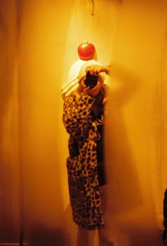 Artistic self-portrait of person with camera, leopard print coat, apple on head in warm tones.