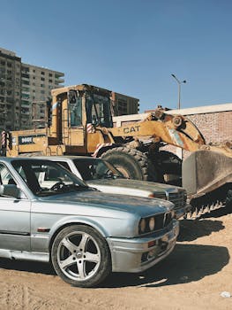 A construction site with a bulldozer and parked cars in an urban area on a sunny day.