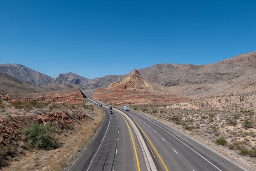 An open highway winding through the striking desert mountains under clear blue skies.