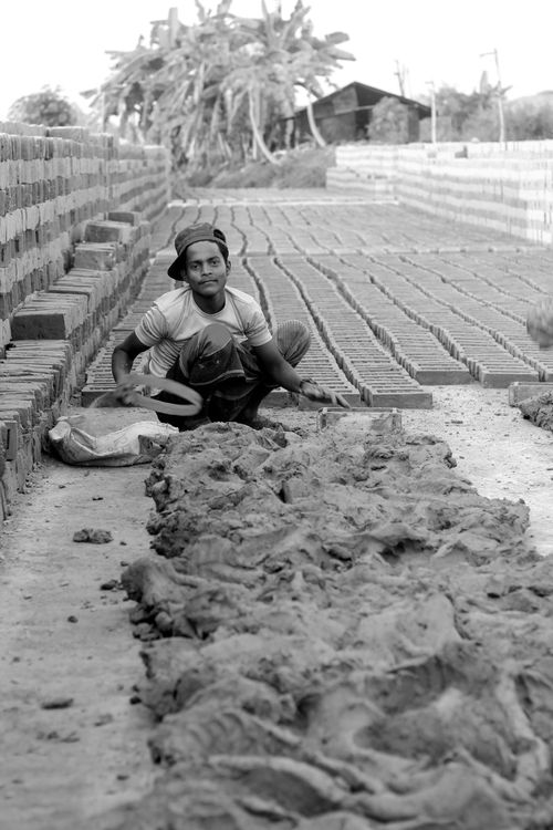 Free A male brickmaker shaping bricks on an outdoor kiln. Monochrome photography enhances the artisanal process. Stock Photo