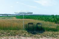Two chairs under a sunshade in a lush field, Attert, Belgium, capturing rural tranquility.