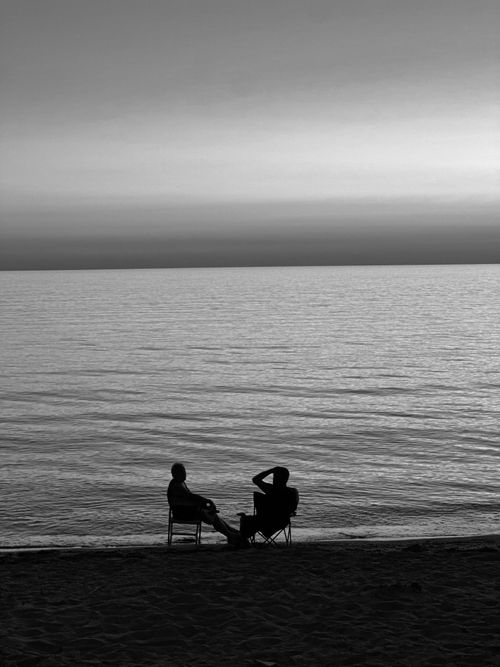 Free Silhouettes of two people seated on a beach at sunset, creating a tranquil seaside scene. Stock Photo