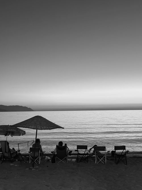 Free Black and white photo of people relaxing on the beach at twilight, creating a peaceful atmosphere. Stock Photo