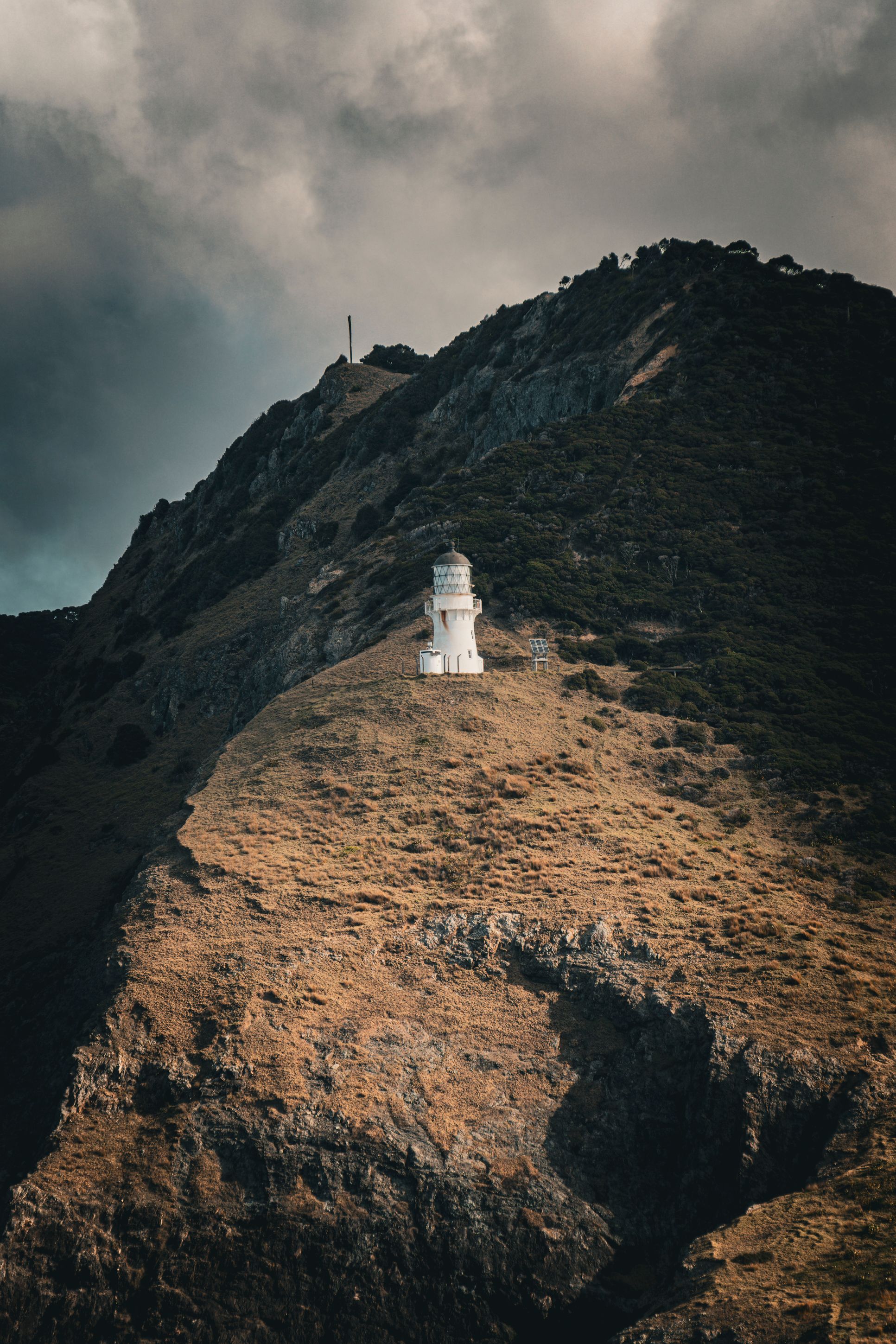 Scenic view of Cape Brett Lighthouse perched on a rugged hillside in Northland, New Zealand under dramatic skies.