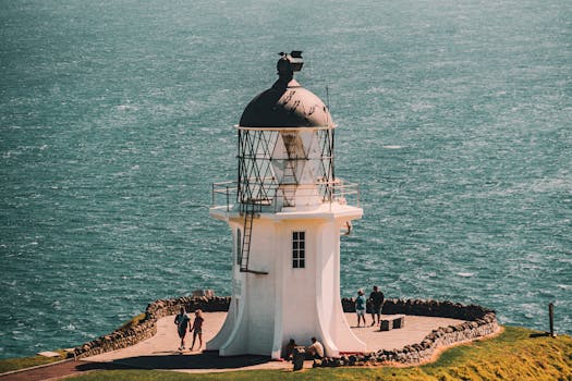 Lighthouse at Cape Reinga overlooking the ocean with tourists enjoying the view.