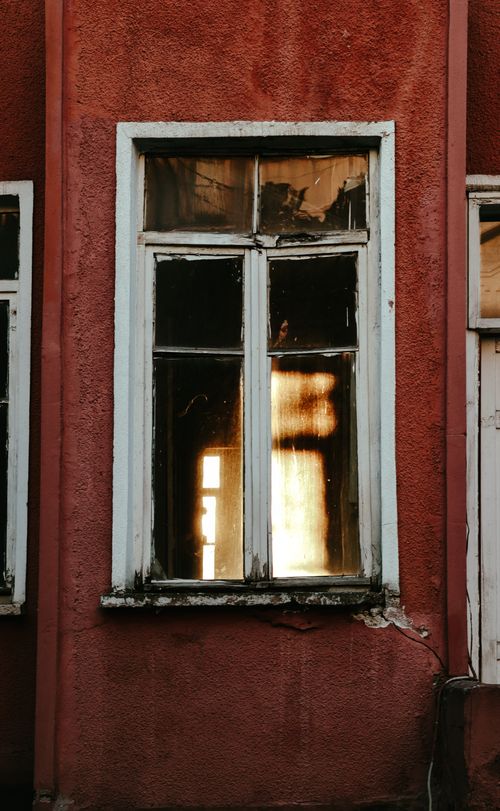 Free An old window with peeling paint reflecting warm light on a red wall Stock Photo