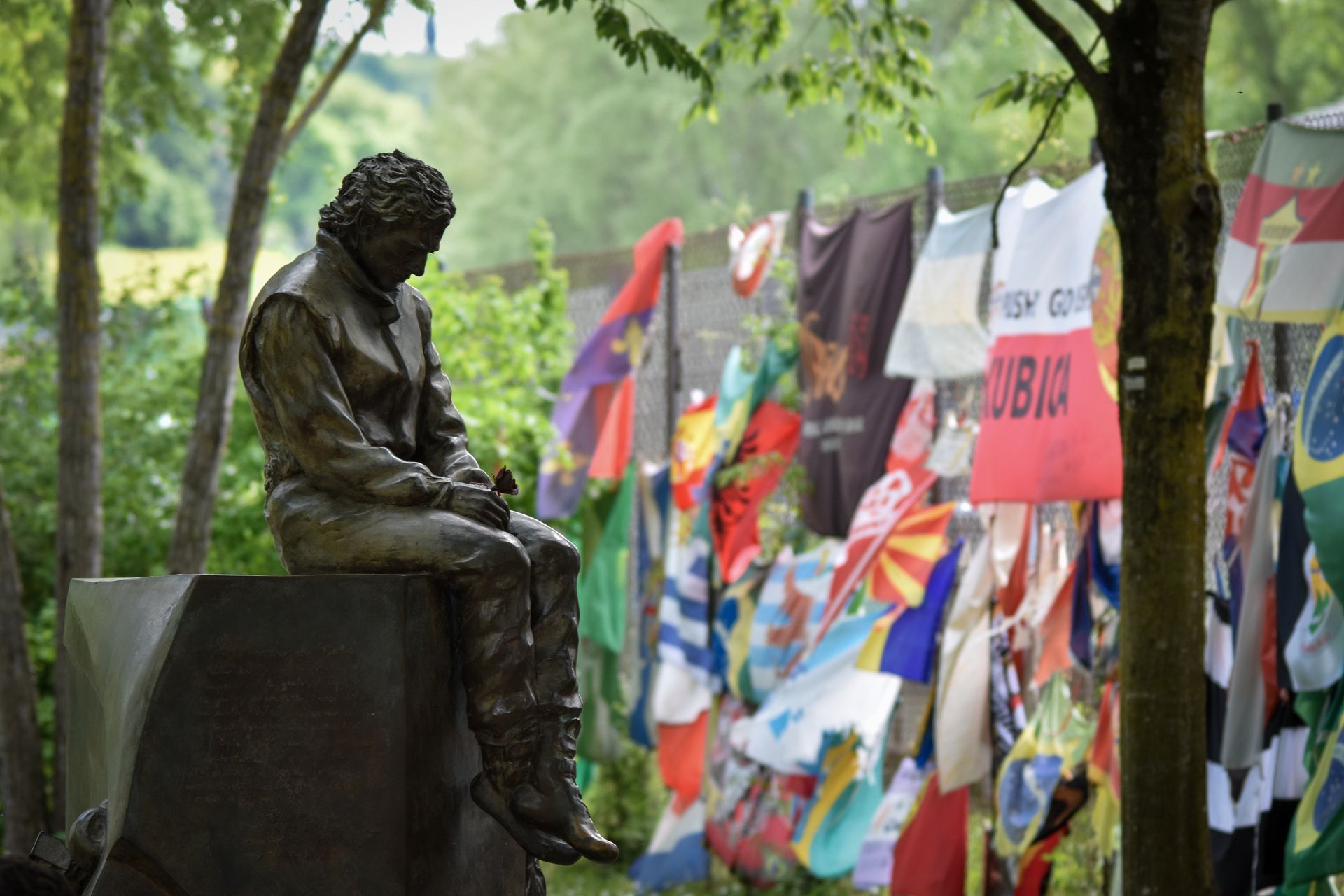 A bronze statue sits beside a display of colorful international flags outdoors.