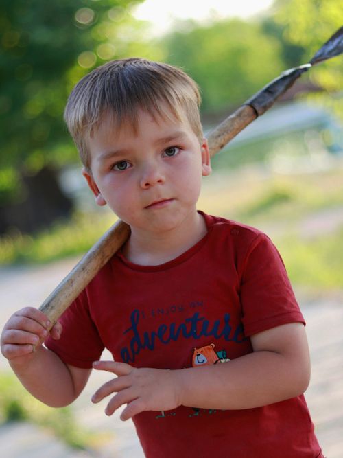 Free Adorable young boy holding a stick outdoors on a sunny day, displaying curiosity and playfulness. Stock Photo