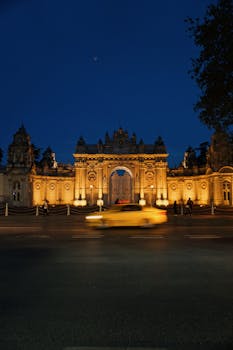 A yellow taxi passes in front of the illuminated Dolmabahçe Palace in İstanbul at night.