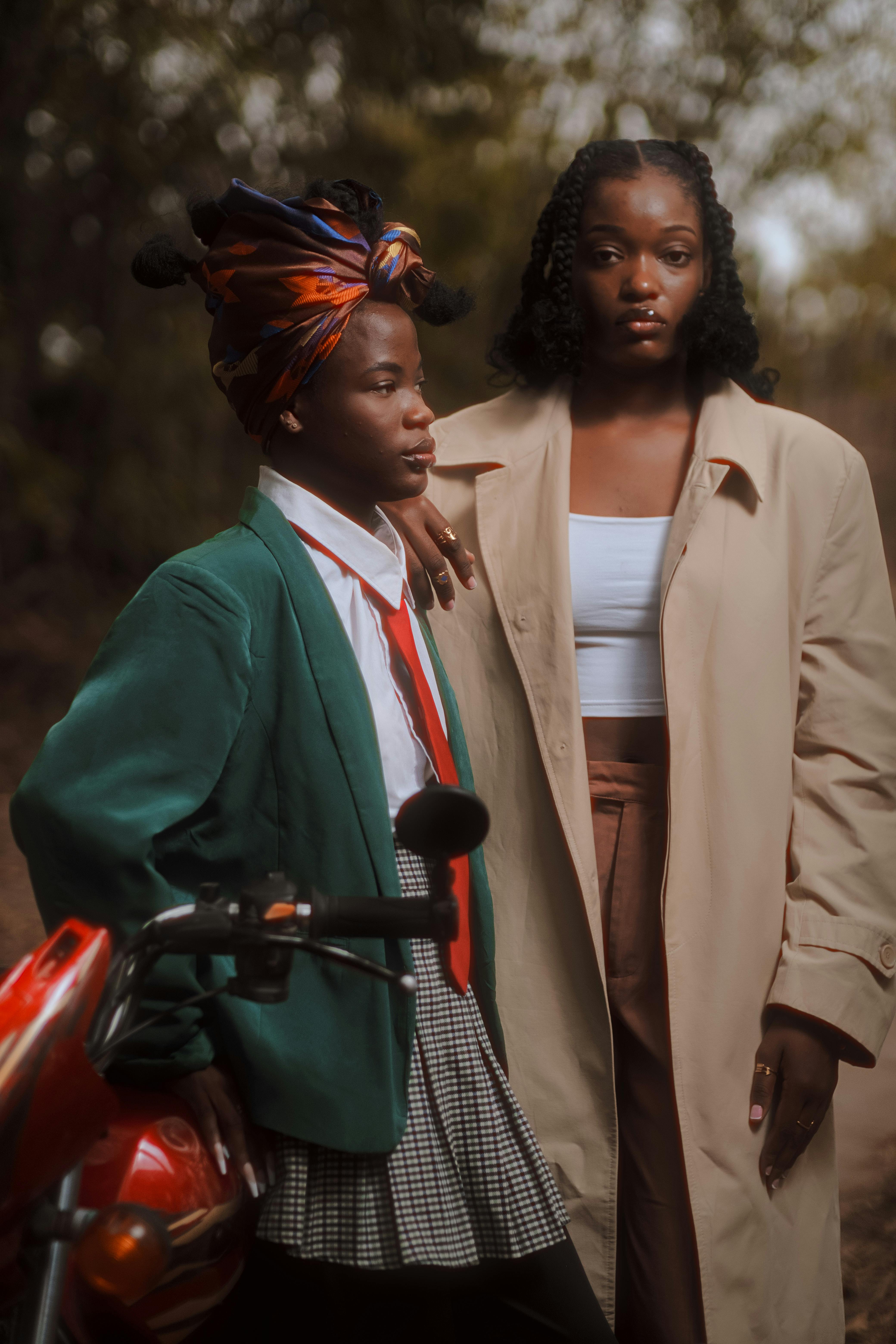 Two stylish individuals pose confidently next to a motorcycle in an urban setting.
