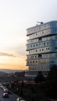 A modern glass building at sunset with a scenic view of cars and nature, offering urban aesthetics.