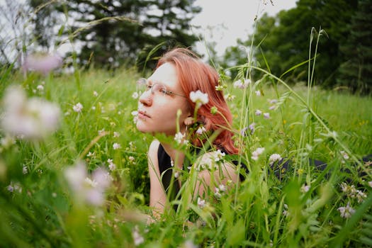 Red-haired woman lying in a vibrant green meadow surrounded by wildflowers, enjoying a peaceful day.