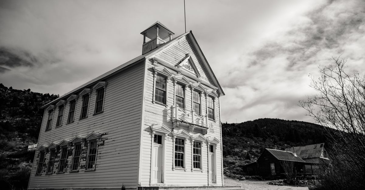 Black and white photo of a historic wooden building in a rural landscape under cloudy skies.