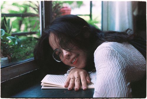 Free A serene moment of a young woman resting by the window with a book, enjoying a peaceful day indoors. Stock Photo
