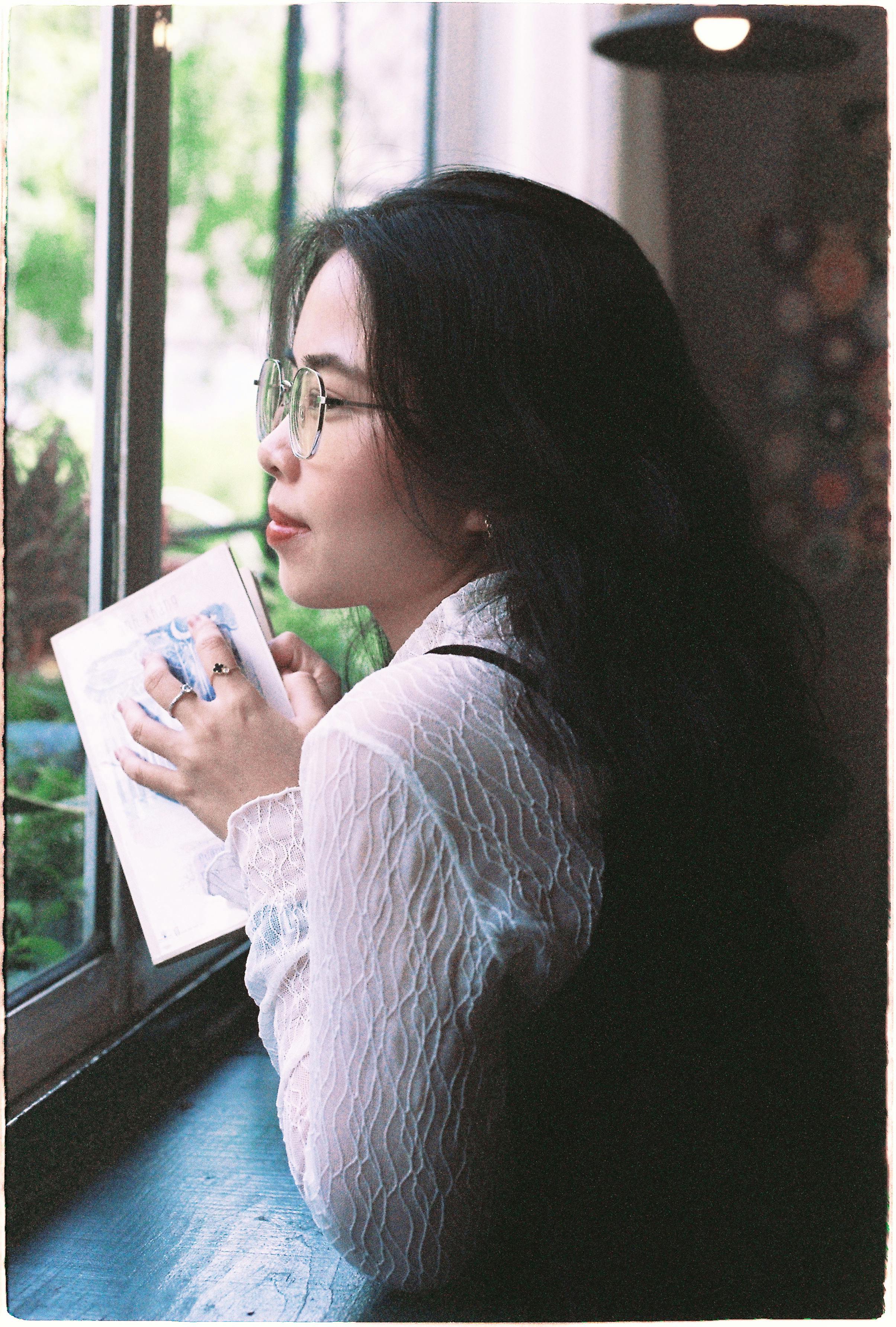 Young woman in glasses reading by a window with soft natural light.