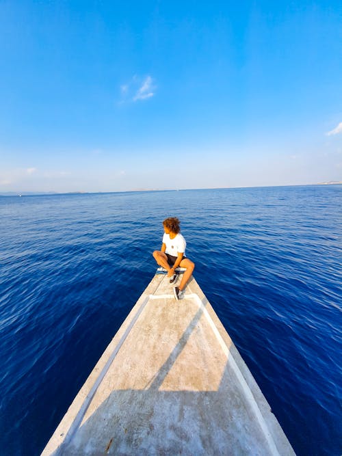 Unrecognizable person sitting at end of narrow pier on seashore