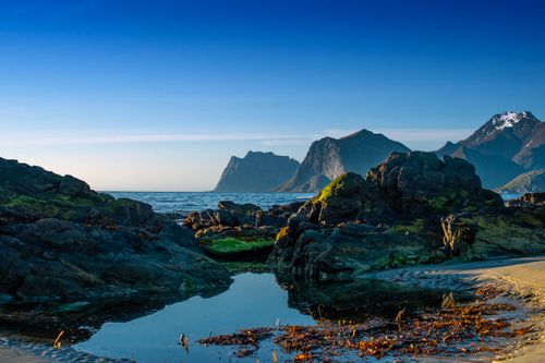 Free Vibrant coastline of Lofoten Islands with rocky beach, clear sky, and mountains in the background. Stock Photo