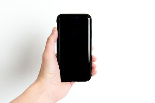 Simple image of a hand holding a black smartphone with a white background, emphasizing minimalism and technology.