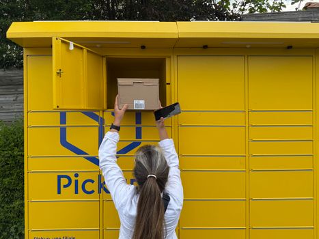 A woman using a yellow parcel locker to pick up a package in Périgueux, France.
