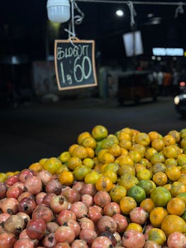 Vibrant oranges and apples stacked in a night market setting with price sign.