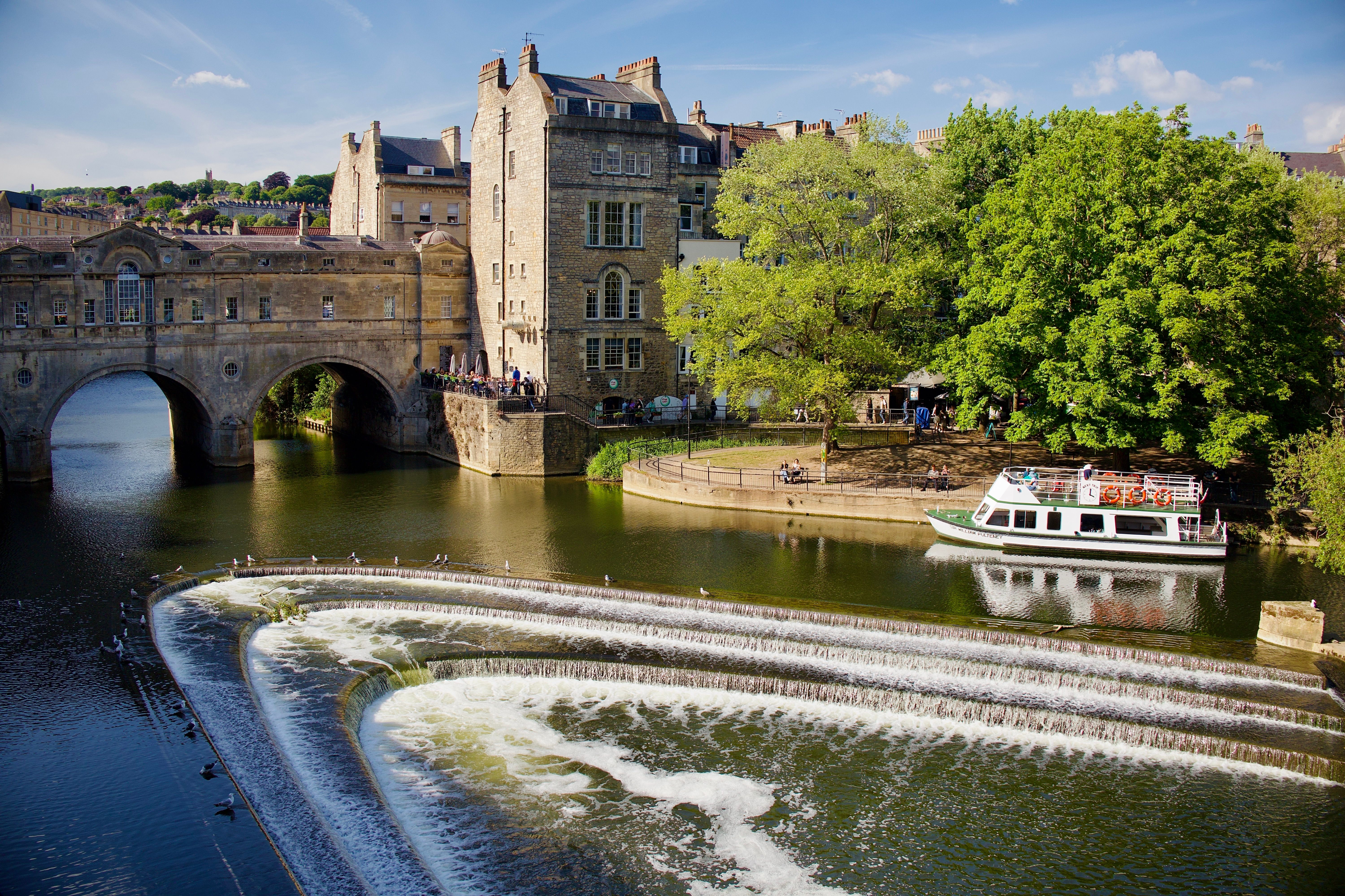 Scenic view of Pulteney Bridge over River Avon with a tour boat and waterfalls. Scenic view of Pulteney Bridge over River Avon with a tour boat and waterfalls.
