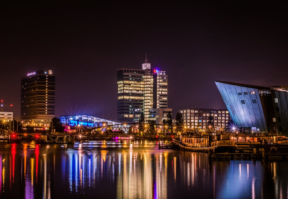 Reflective night view of Amsterdam's modern skyline by the water.