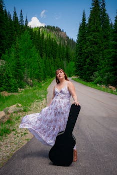 Woman in a floral dress with a guitar case in scenic Colorado mountain landscape.
