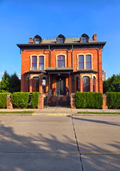 A beautiful red brick Victorian-style house with lush greenery and clear blue sky.