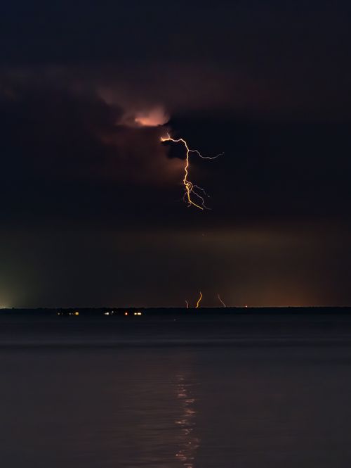 Free A striking view of lightning over Santa Rosa Beach, Florida, captured at night with reflections on the calm water. Stock Photo