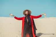 阳光明媚的沙漠中，一名身穿红色外套、头戴帽子的女子开心地微笑着