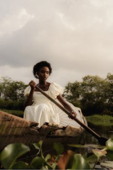 A tranquil scene of an African woman rowing a canoe through serene waters, reflecting nature's beauty.