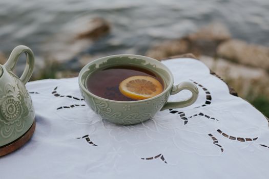 Elegant teacup with lemon slice by lakeside, capturing a peaceful outdoor setting.