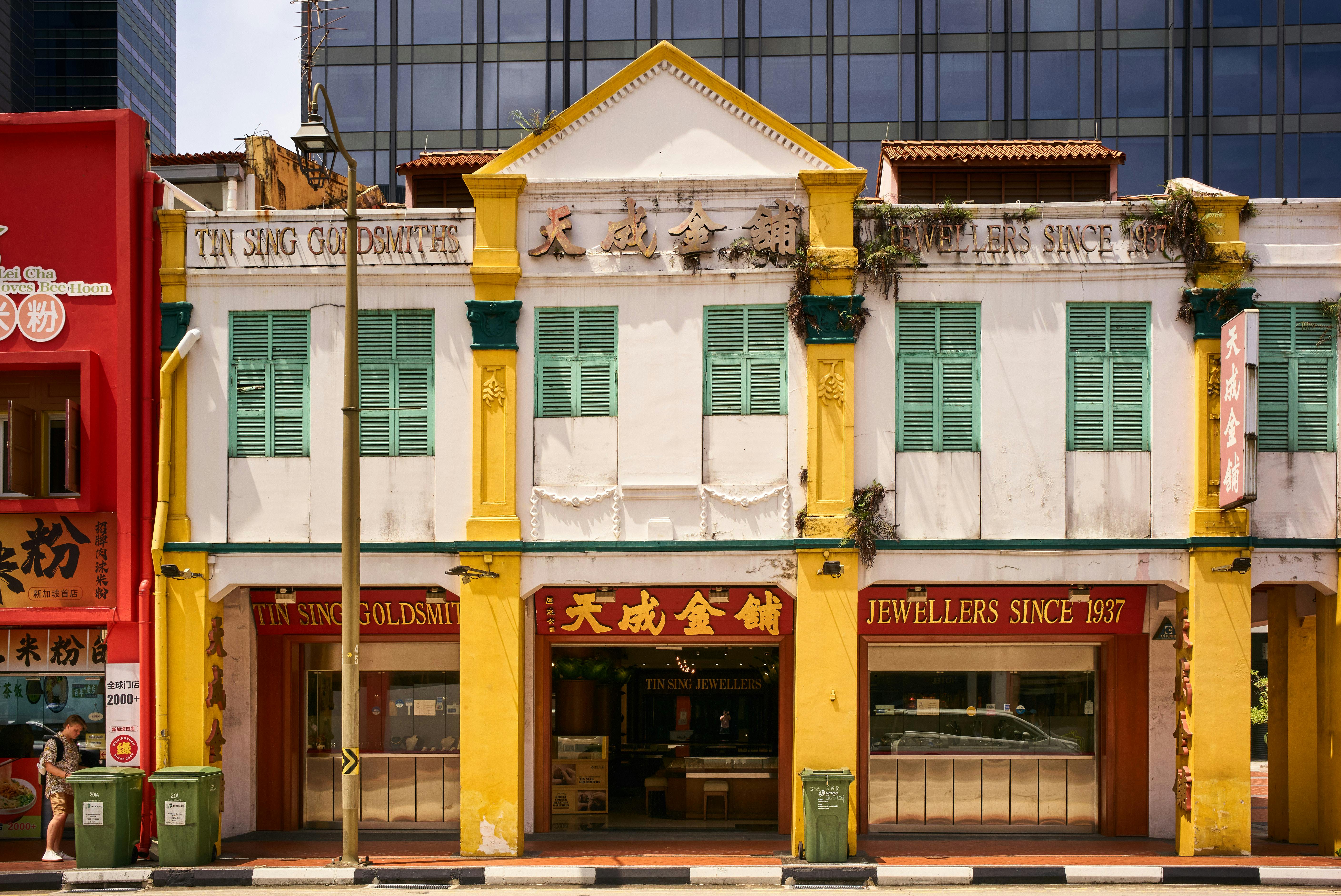 Vibrant shophouse with historical architecture amidst modern buildings.
