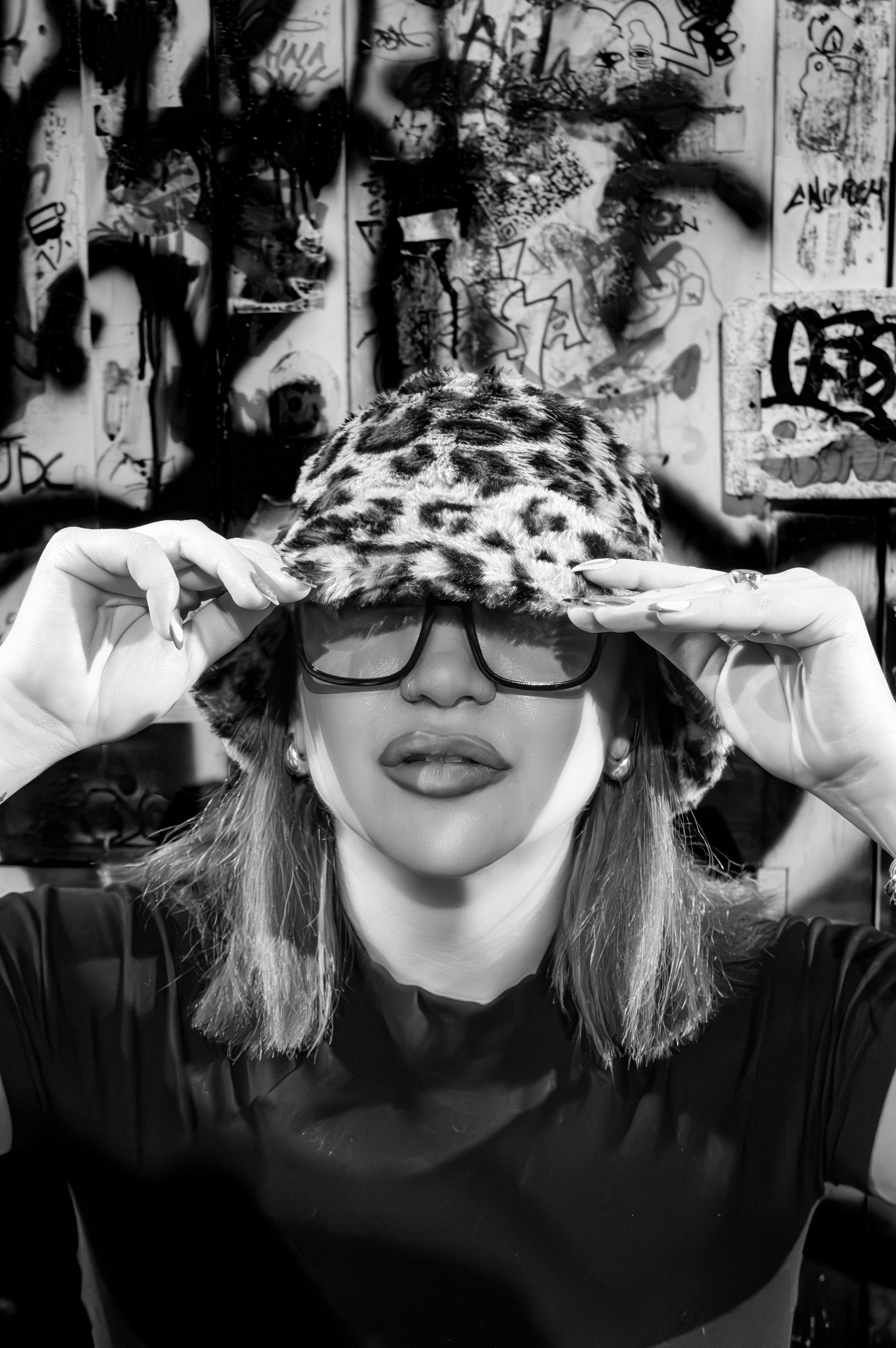 bezplatná Černobílý portrét ženy pózující s leopardím kloboukem a slunečními brýlemi v městském prostředí. Základová fotografie