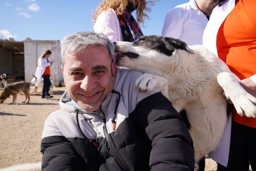 A joyful moment captured of a man being licked by a dog outdoors in a sunny setting, showcasing human-animal bond.