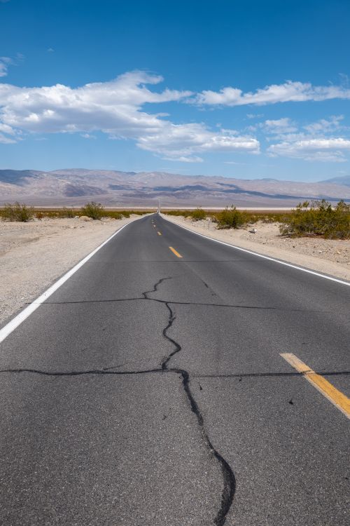 Free A desolate road stretches endlessly through Death Valley National Park under a blue sky. Stock Photo