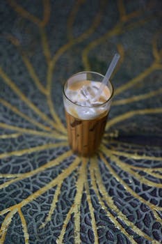 Glass of iced coffee with a straw on a colorful mosaic table, perfect for refreshing summer vibes.