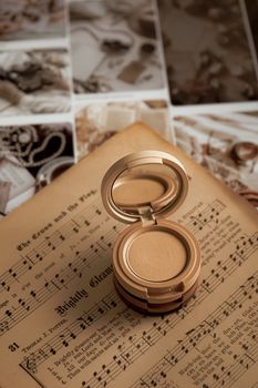 A vintage makeup compact sits open on an antique sheet music page, creating a nostalgic aesthetic.