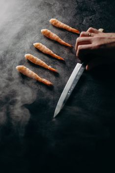 An elegant display of shrimp and knife on a dark surface, capturing culinary art.