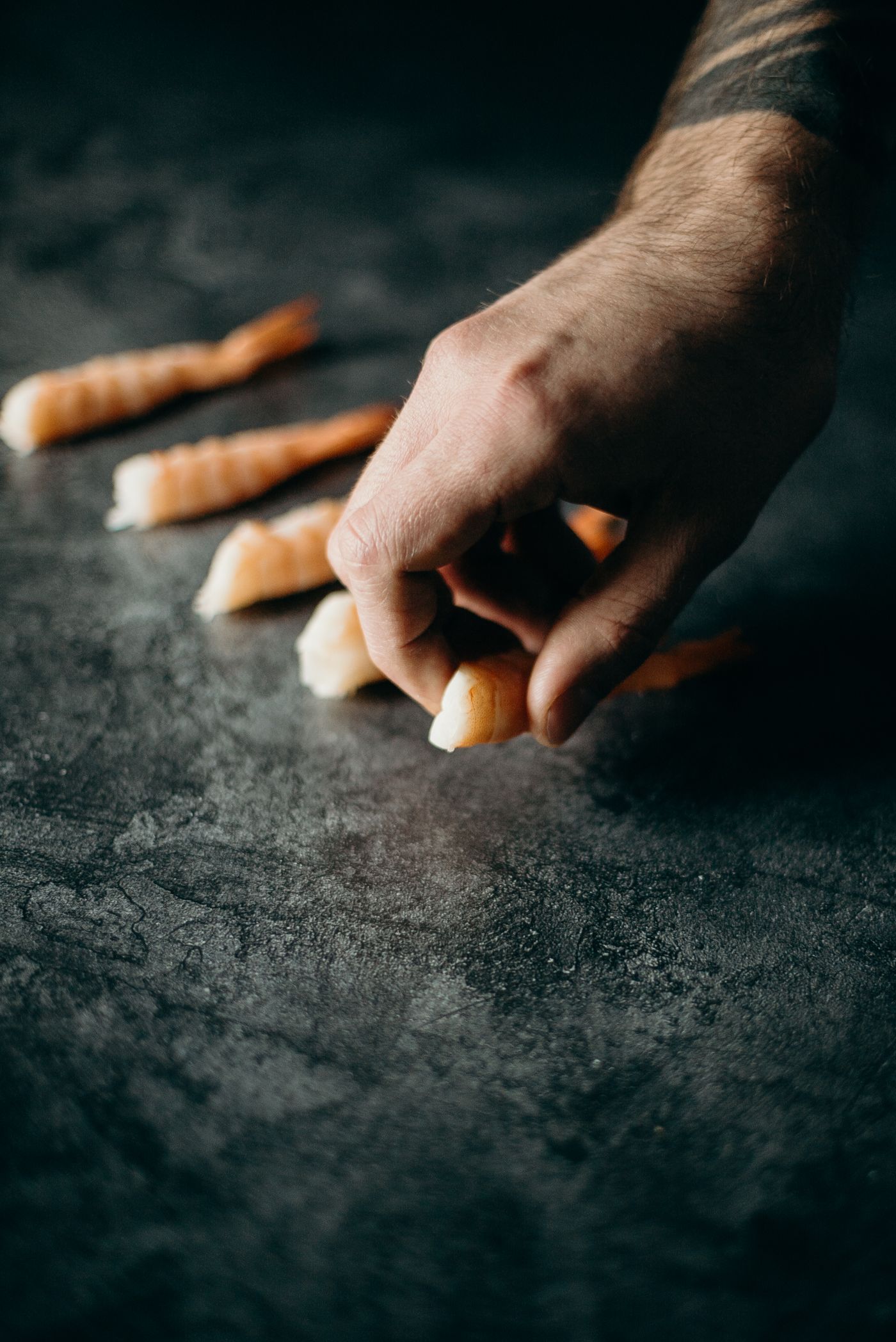 Hands arranging fresh prawns on a dark surface