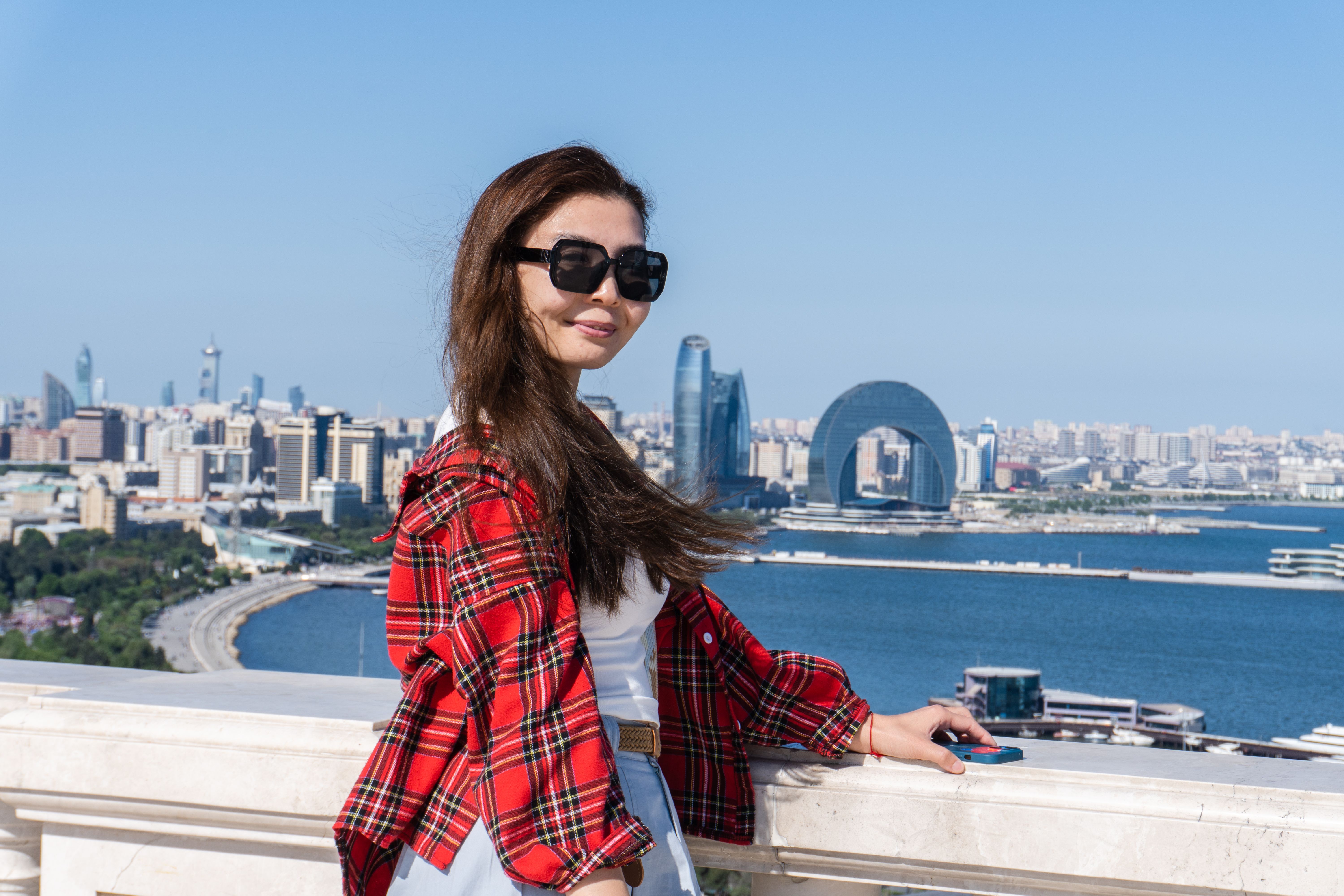 Young woman in sunglasses with Baku skyline in the background, capturing urban beauty and travel lifestyle.
