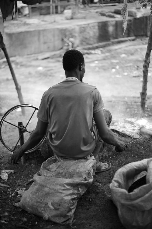 Free Black and white photo of an artisan sitting outdoors working with a spinning wheel. Stock Photo