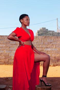 Confident woman in vibrant red dress posing outdoors with brick wall backdrop.