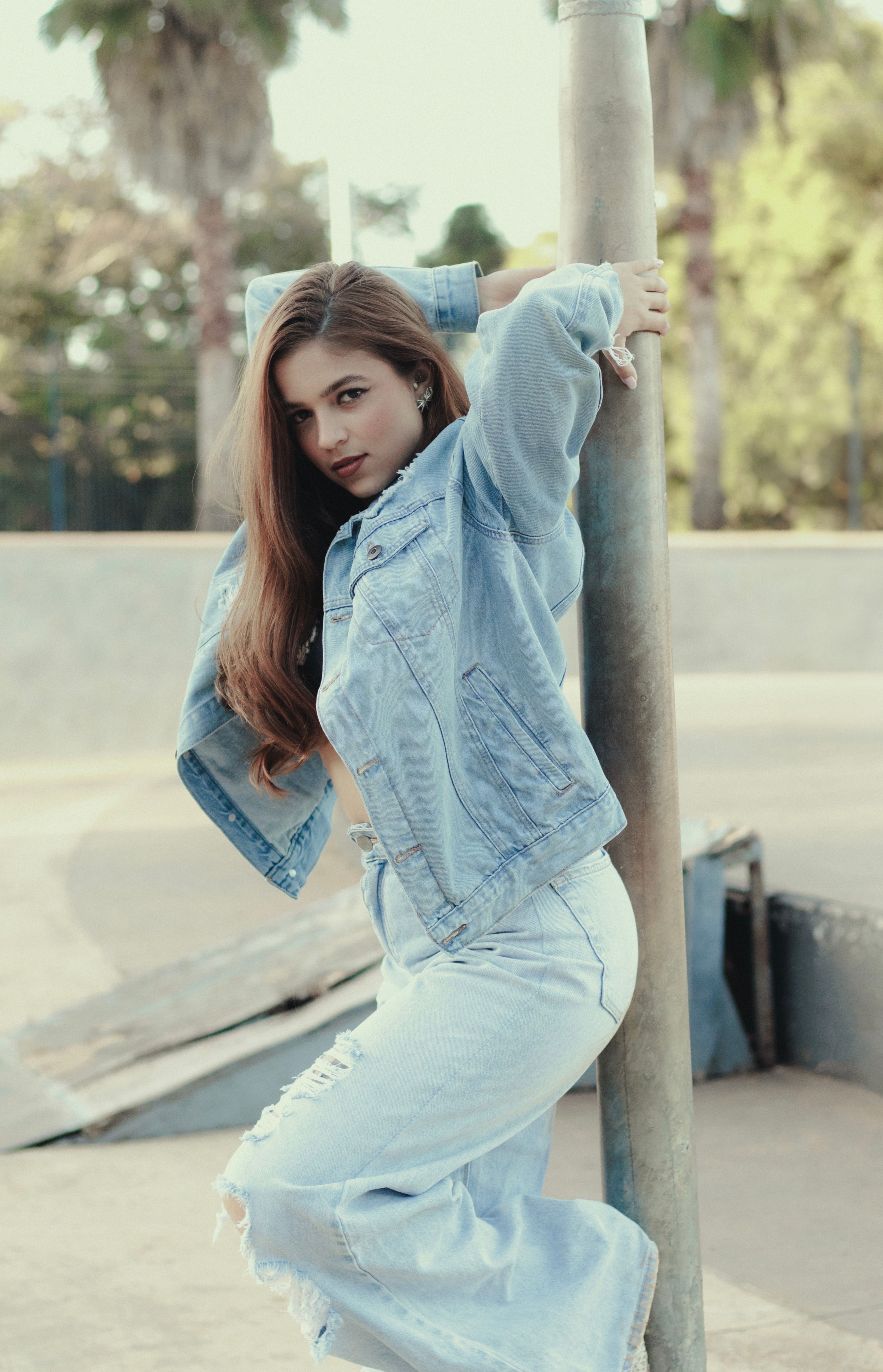 Stylish young woman striking a pose in a denim outfit at a sunny skate park in Goiânia, Brazil.