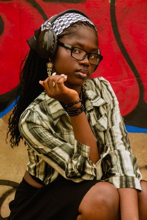 Free Woman wearing headphones and glasses, posing confidently against an urban graffiti background. Stock Photo